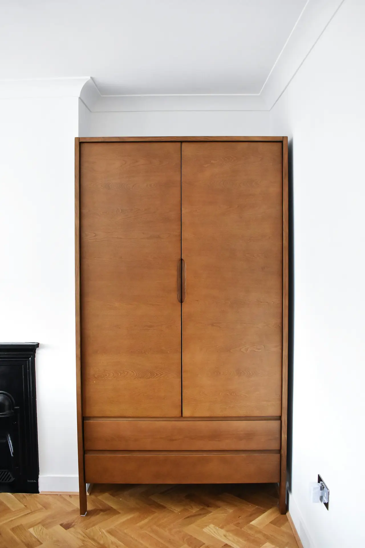 A freestanding wooden wardrobe against a white wall